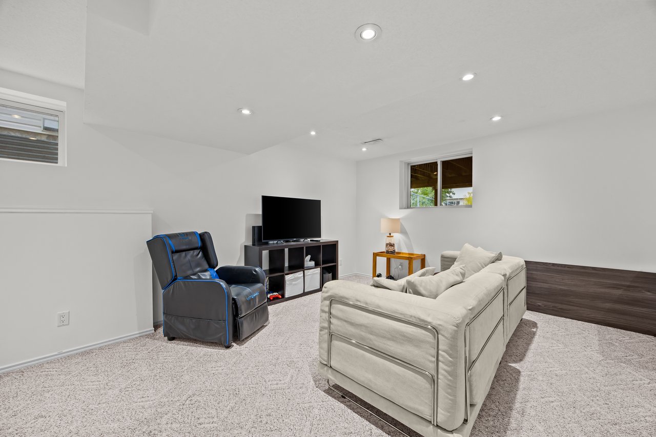 Furnished basement family room with a white sectional, blue-trimmed recliner, and television.