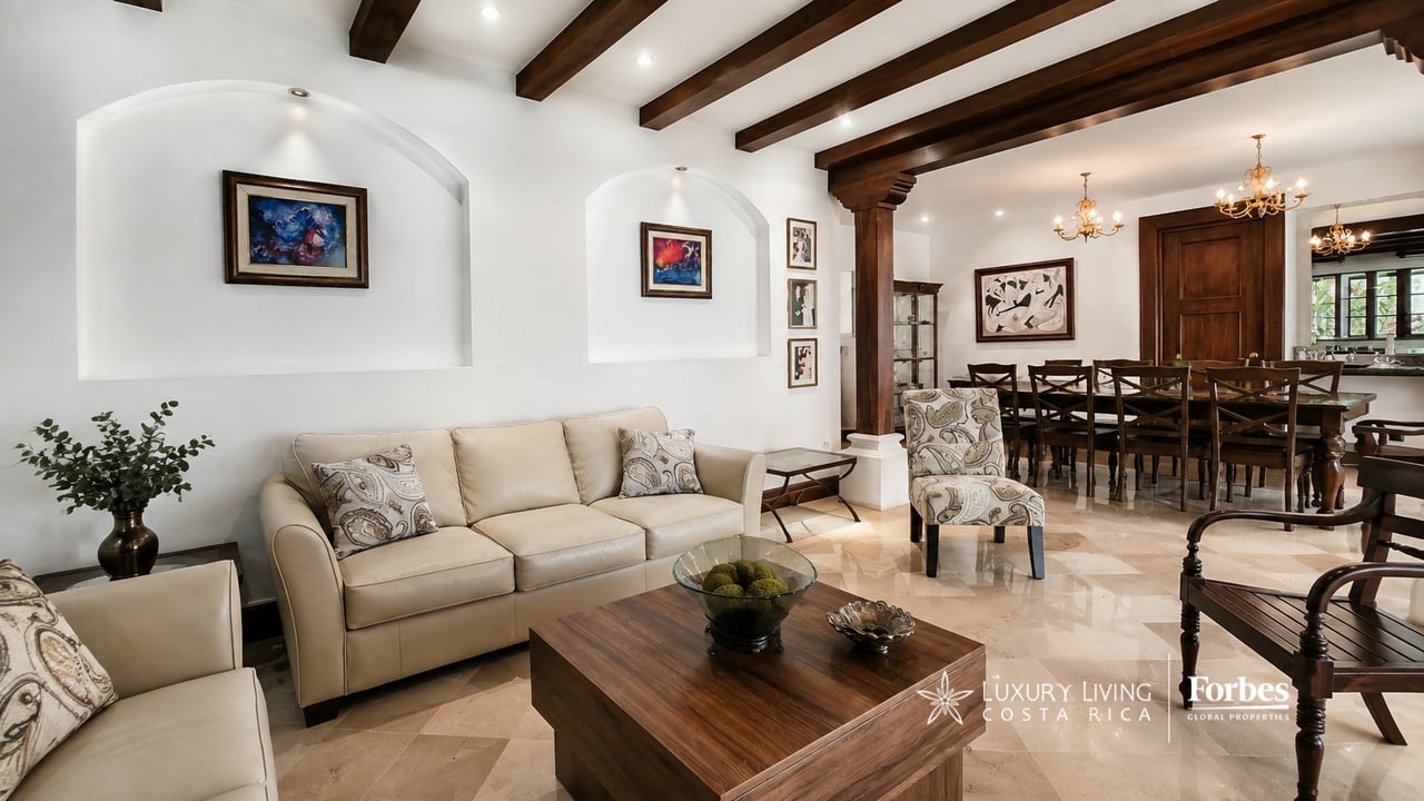 Living and dining room with cream sofas, dark wood beams, and a long dining table.