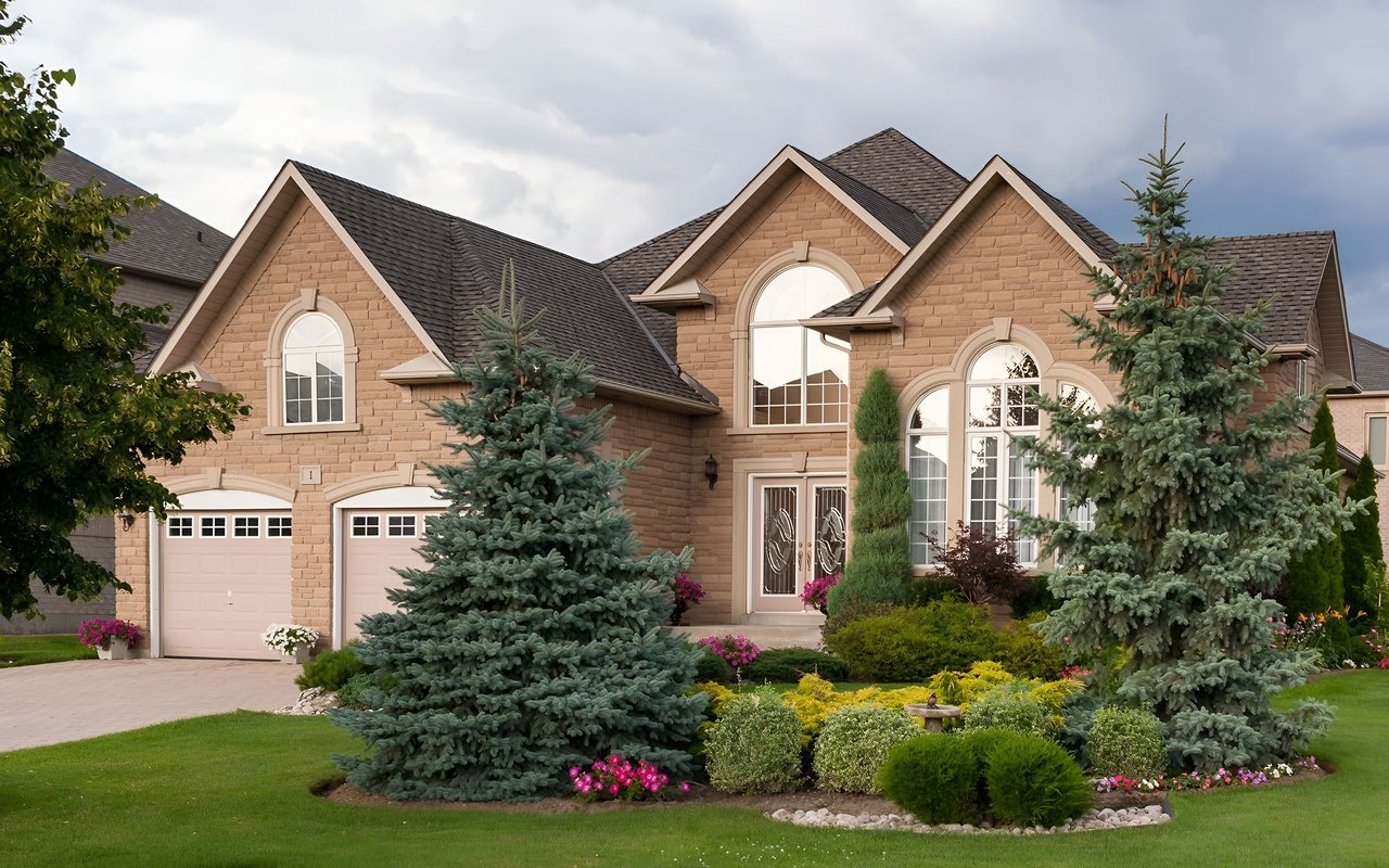 Tan brick house with arched windows, two garages, and a landscaped front yard.