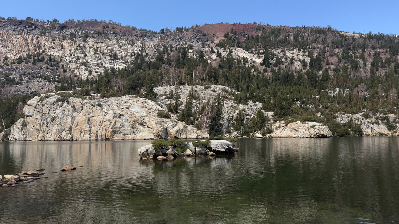Mountain lake and rocky island below forested granite cliffs near Mammoth Lakes.