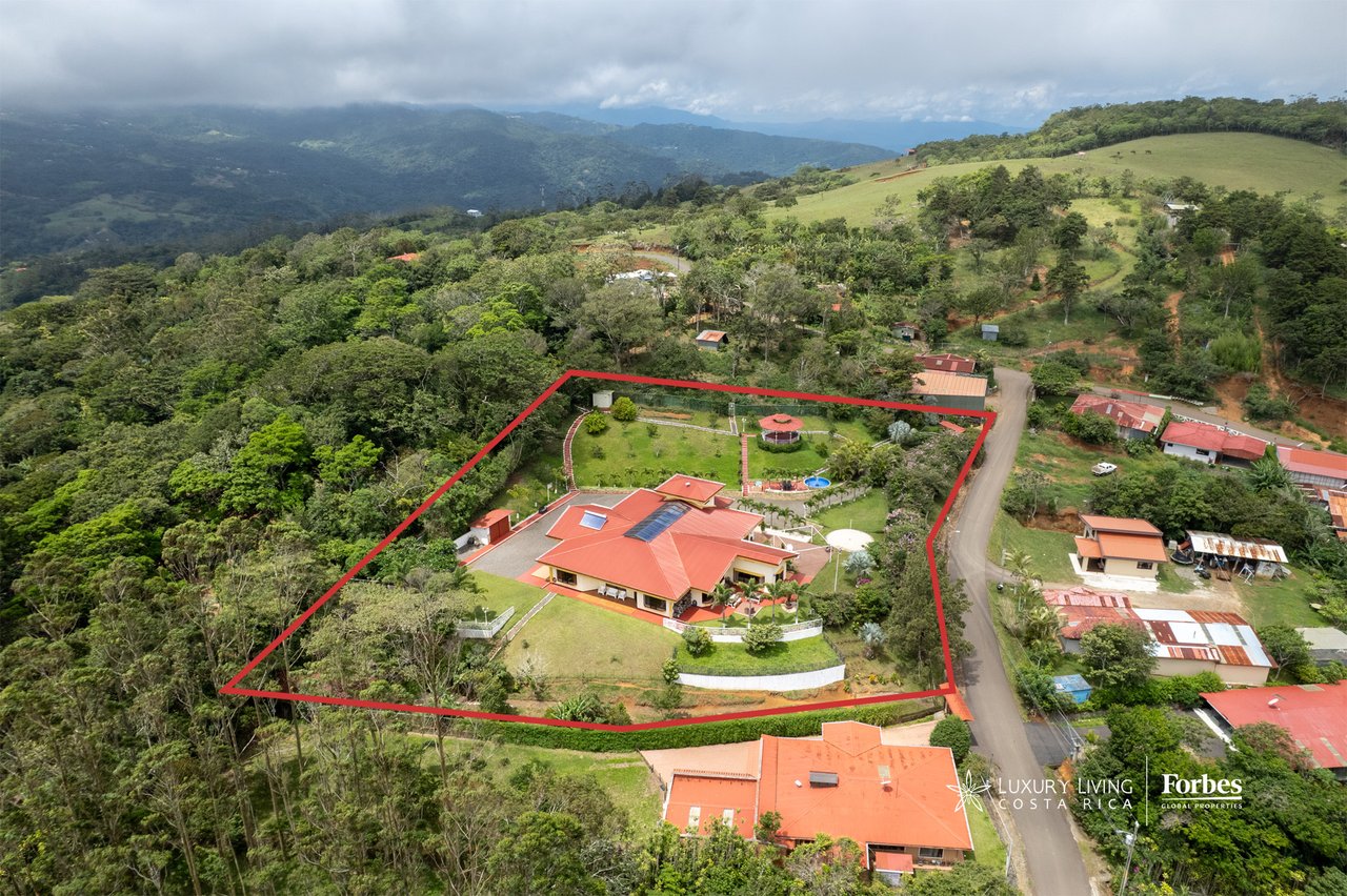 Aerial view of red-roofed home and landscaped grounds outlined in red, backed by forested mountains.