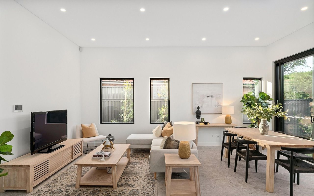 Open-plan living and dining room with a gray sectional, light wood furniture, and large windows.