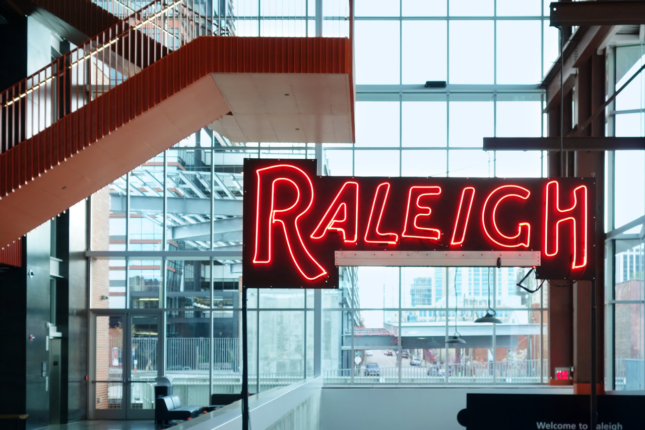 Neon Raleigh sign inside a modern glass atrium.
