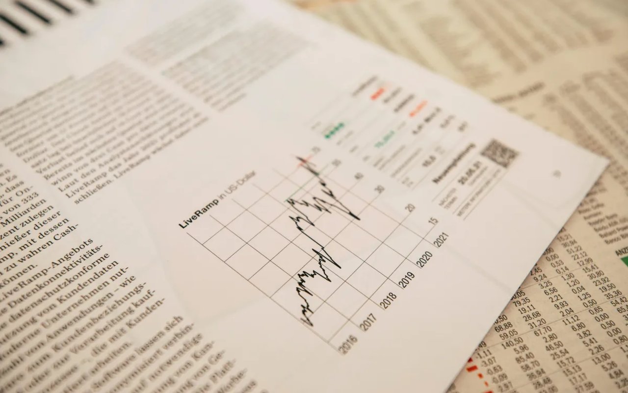 A financial newspaper or document is shown, with a line graph illustrating stock performance over several years.