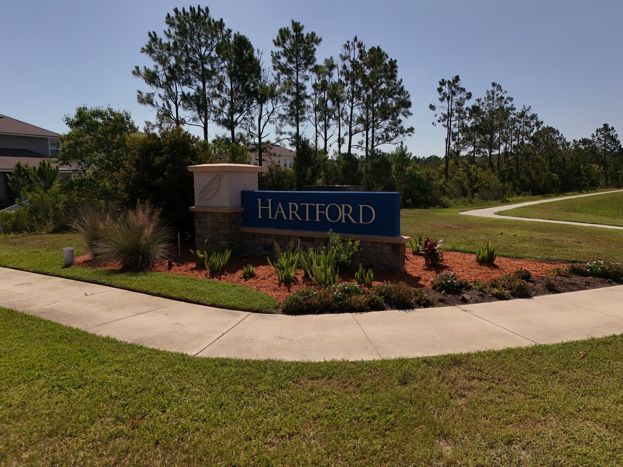 Hartford community entrance sign amid landscaped beds, pine trees, and nearby homes.