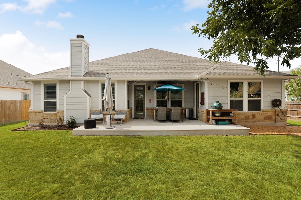 Home’s rear patio with outdoor seating and grill overlooking a green lawn.