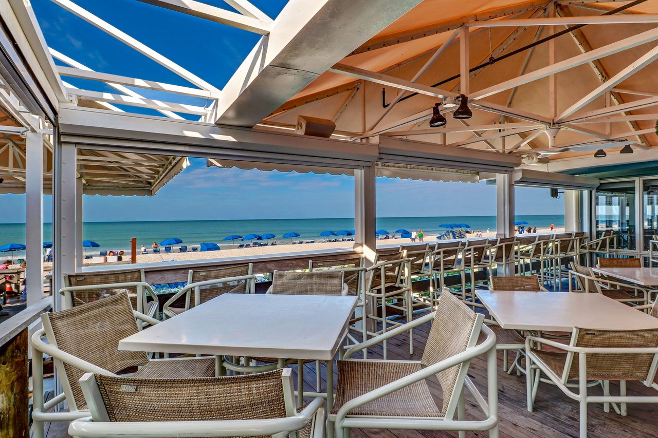 Beachfront restaurant terrace with woven chairs and tables overlooking the beach and Gulf.