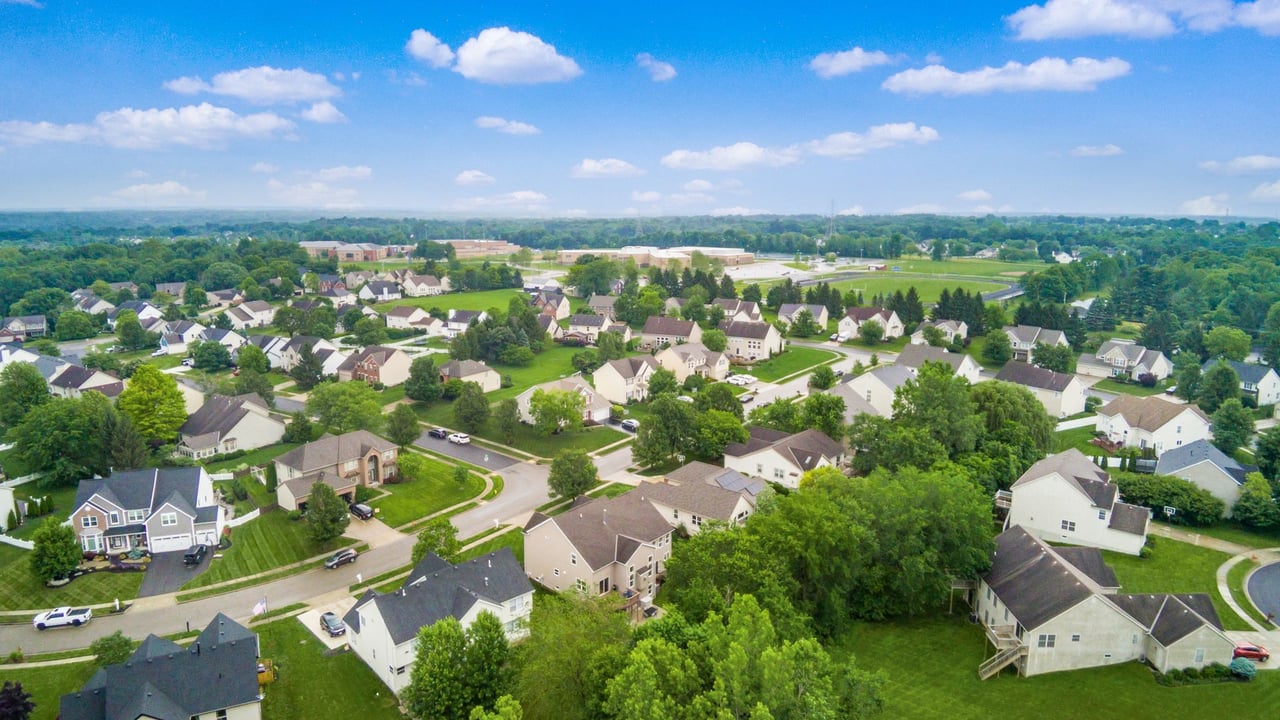 Aerial drone view of Lewis Center Ohio 43035 neighborhood with newer construction homes, tree-lined streets, and Olentangy Orange High School visible in the background