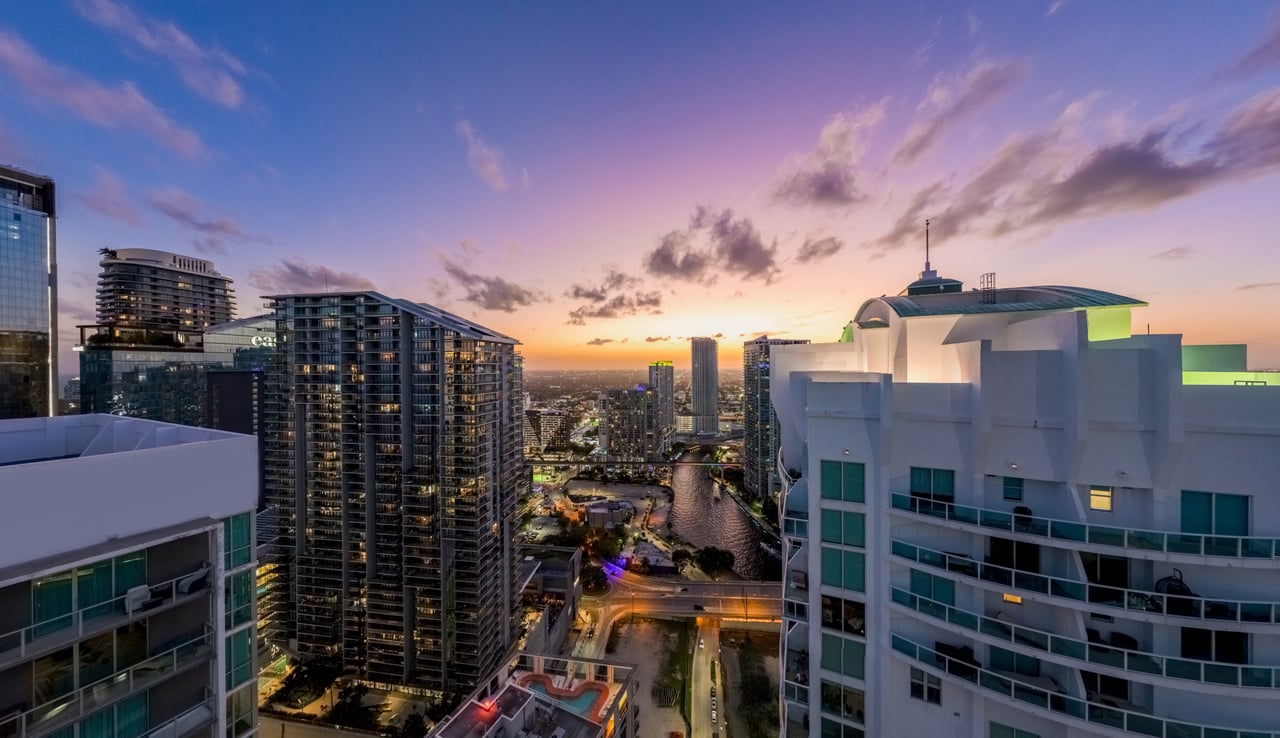 Downtown Miami skyline and waterway at dusk, viewed between high-rise buildings.