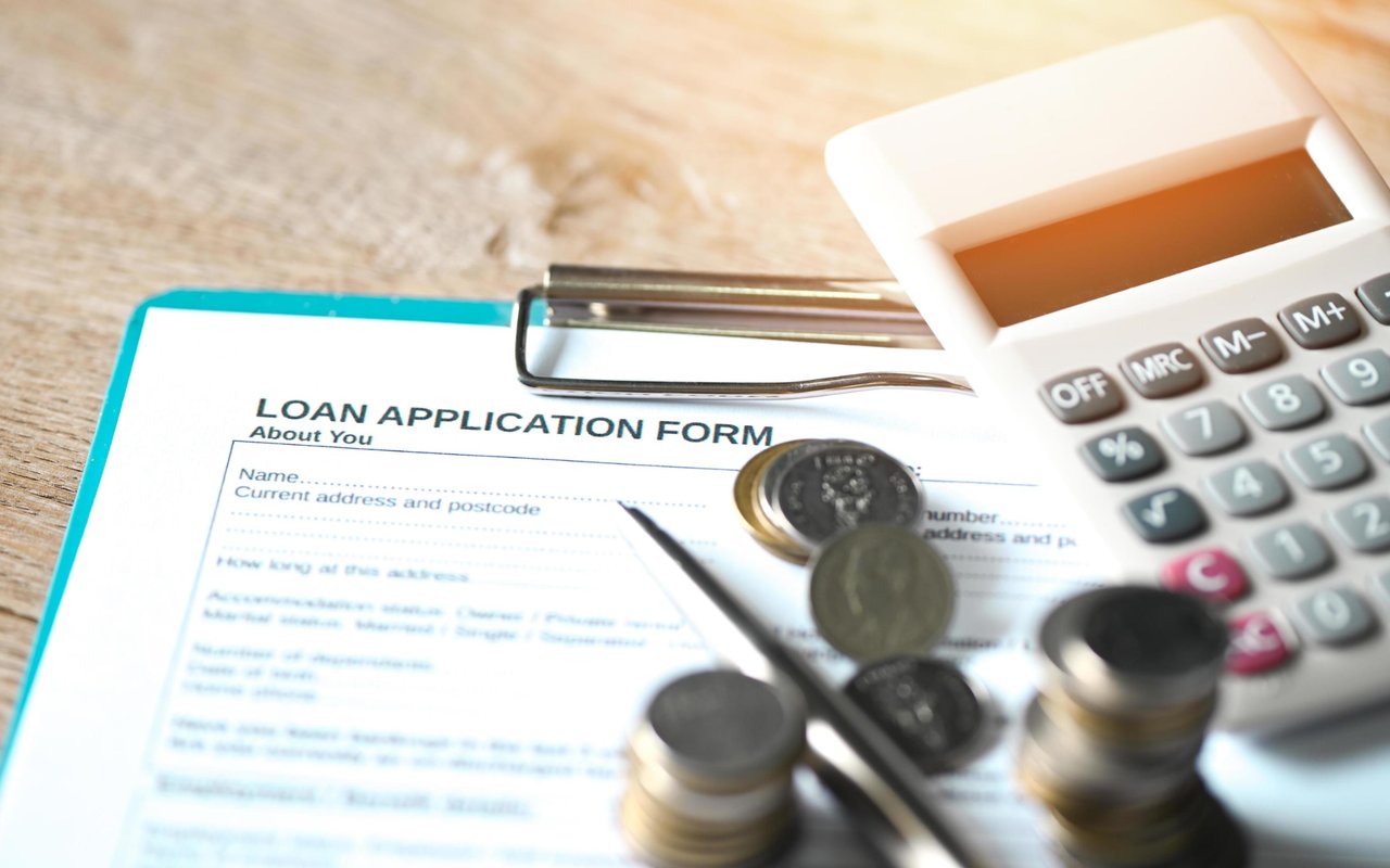 Loan application form with a calculator, pen, and coins.