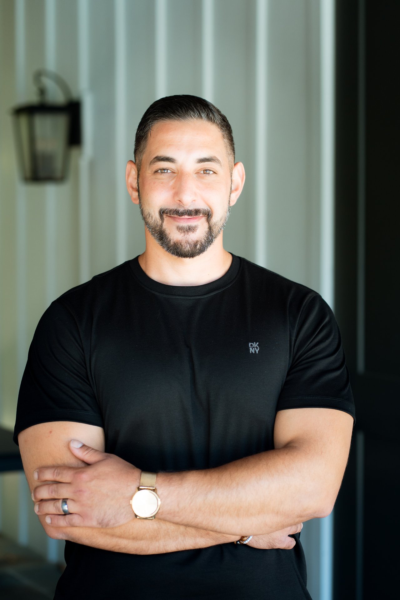Wesam Hamad standing with arms crossed in a black shirt, wearing a watch.