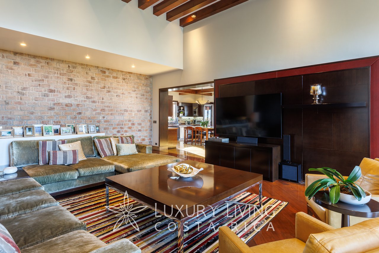 Living room with a large sectional, exposed brick wall, dark wood TV unit, and colorful striped rug.