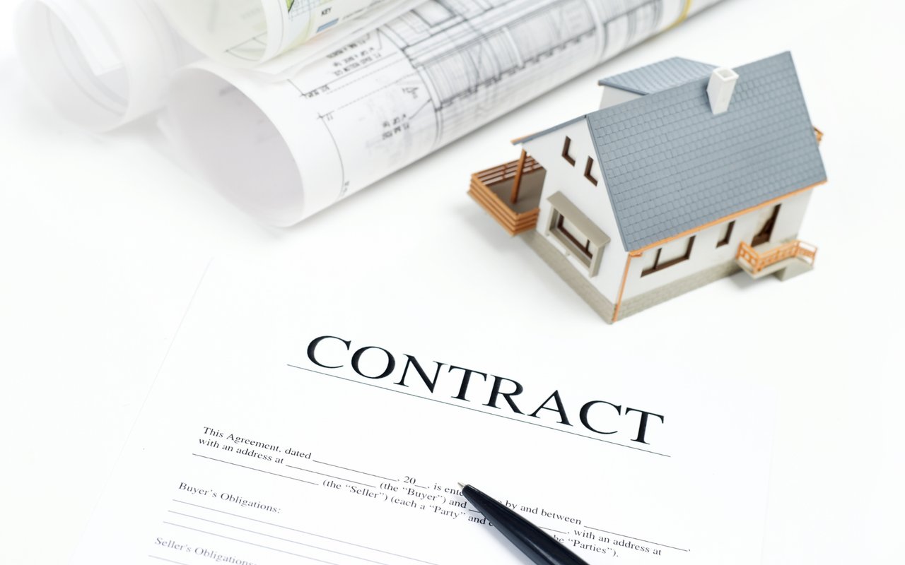 Miniature house on a contract, with rolled architectural plans and a pen.
