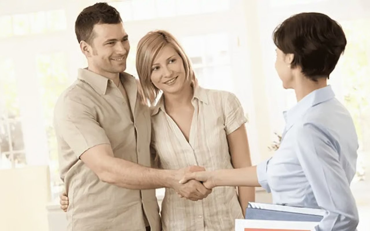 A couple shakes hands with a real estate agent during a bright indoor meeting.
