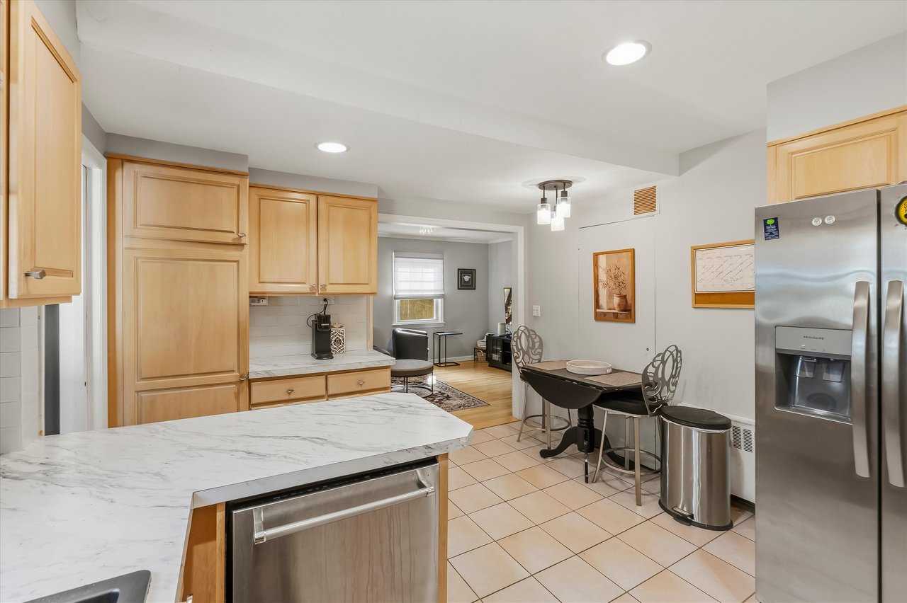Kitchen with a marble-look island, light wood cabinets, and an adjoining dining and sitting area.
