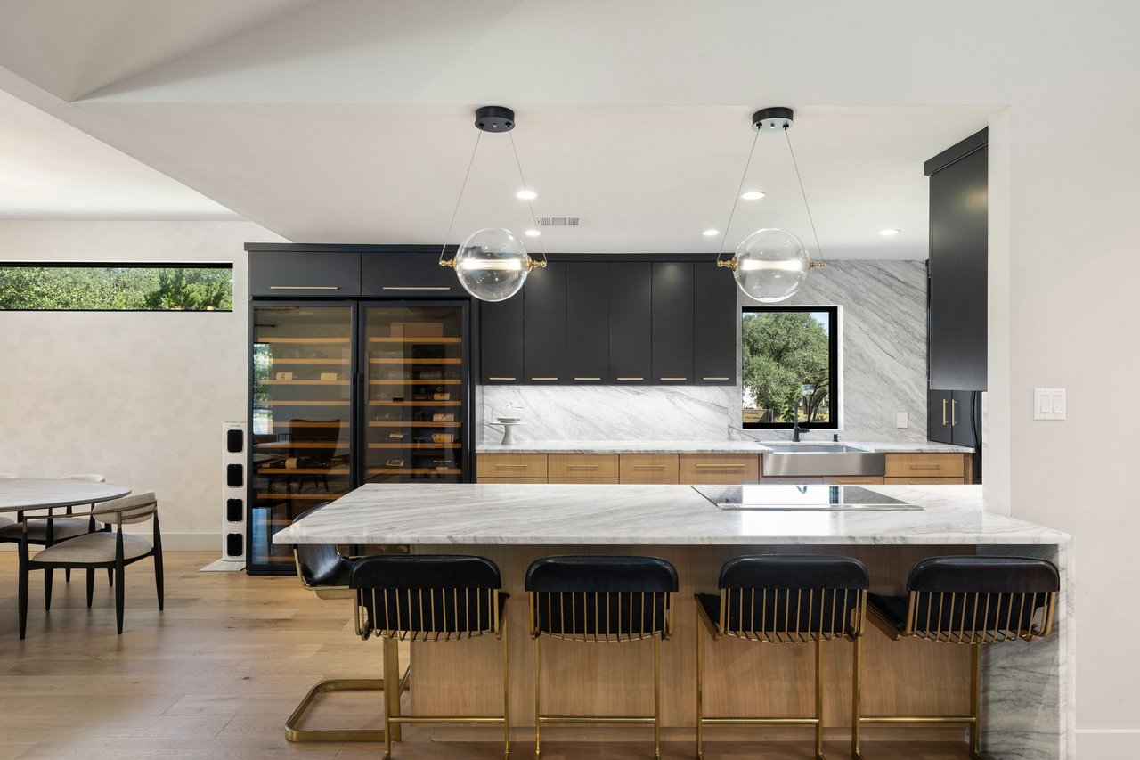 Modern kitchen with a marble island, charcoal cabinets, wood cabinetry, and glass-front wine refrigerators.