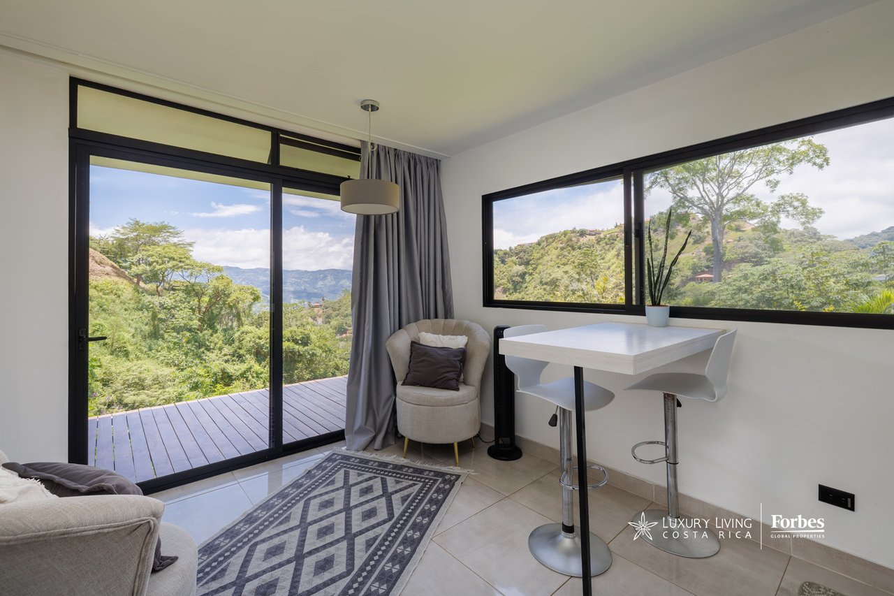 Dining nook with large windows overlooking a wooden deck and green mountain views.