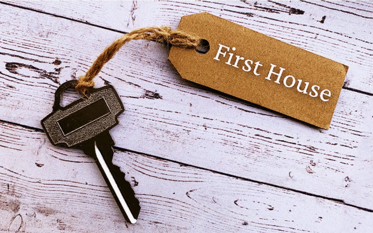 House key beside a tag reading “First House” on whitewashed wood.