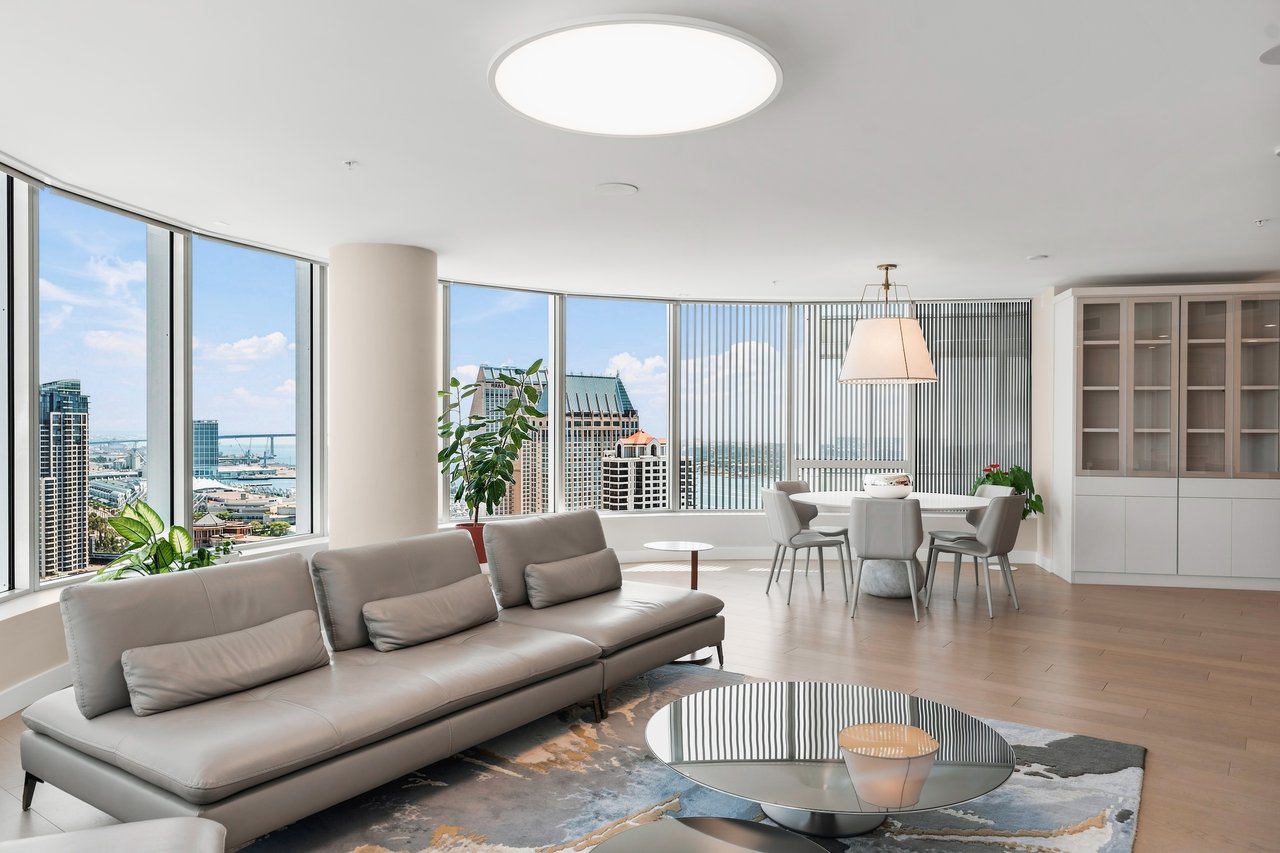 High-rise condo living room with a gray sectional and panoramic windows overlooking downtown and the waterfront.