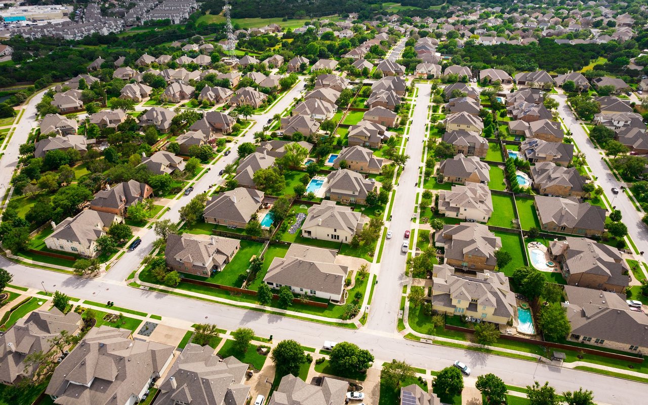 Aerial view of a Round Rock neighborhood with tree-lined streets, green yards, and backyard pools.