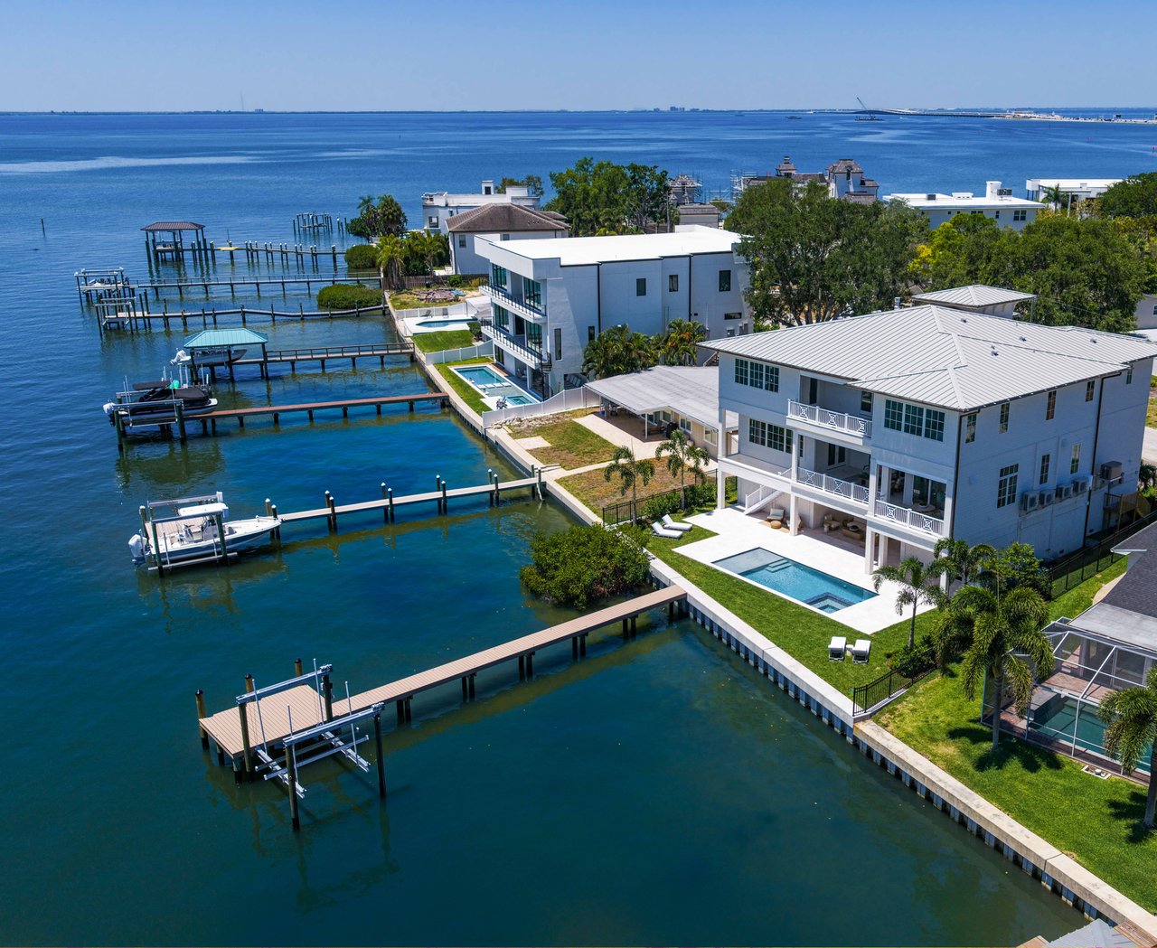 Aerial view of modern waterfront homes with private docks and a pool beside the bay.