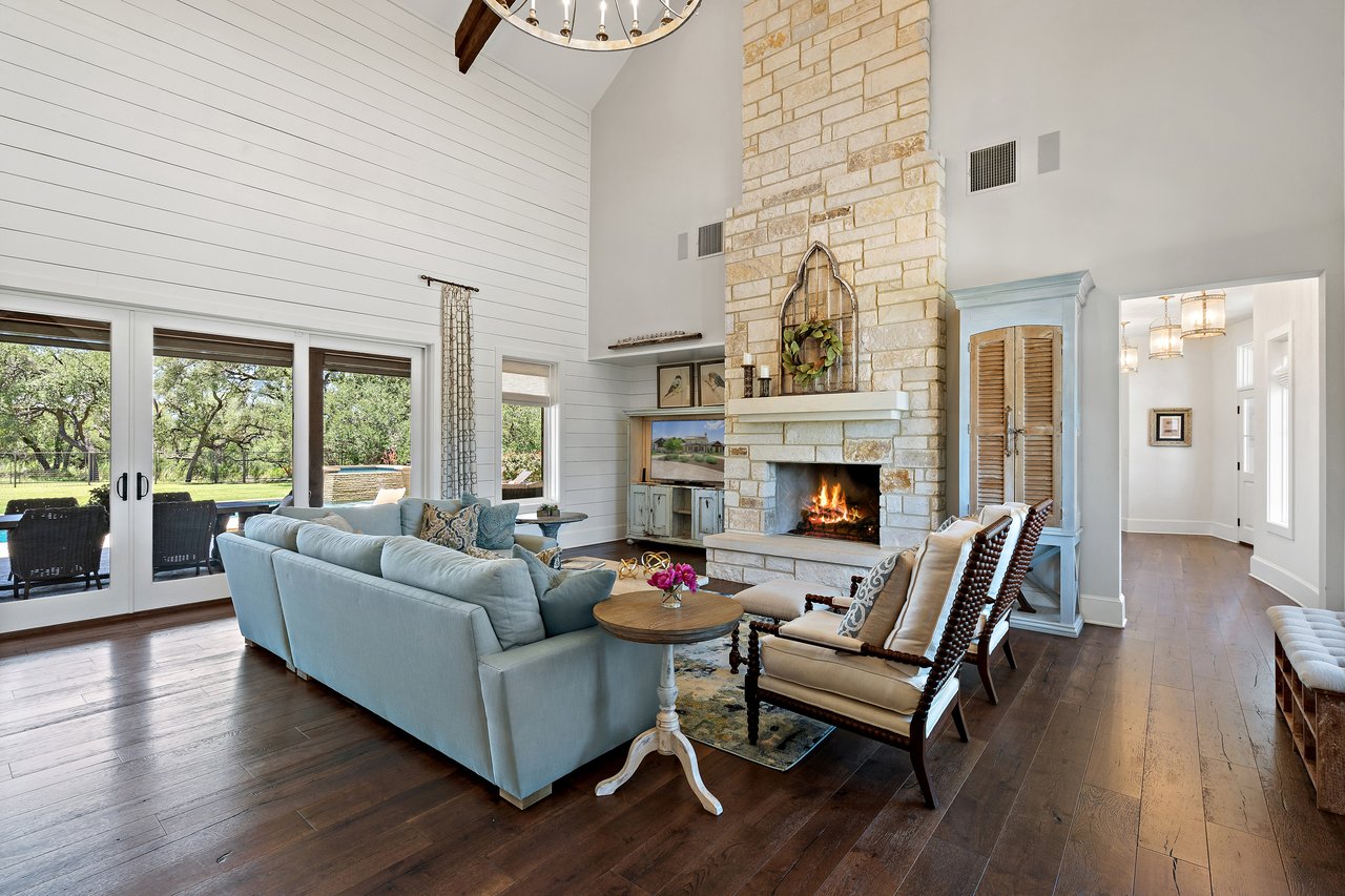 Living room at 335 Winning Colors with a floor-to-ceiling limestone fireplace and French doors opening toward the pool.