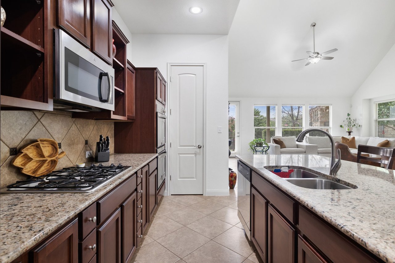 Kitchen with dark wood cabinets and granite counters, opening to a bright living area.