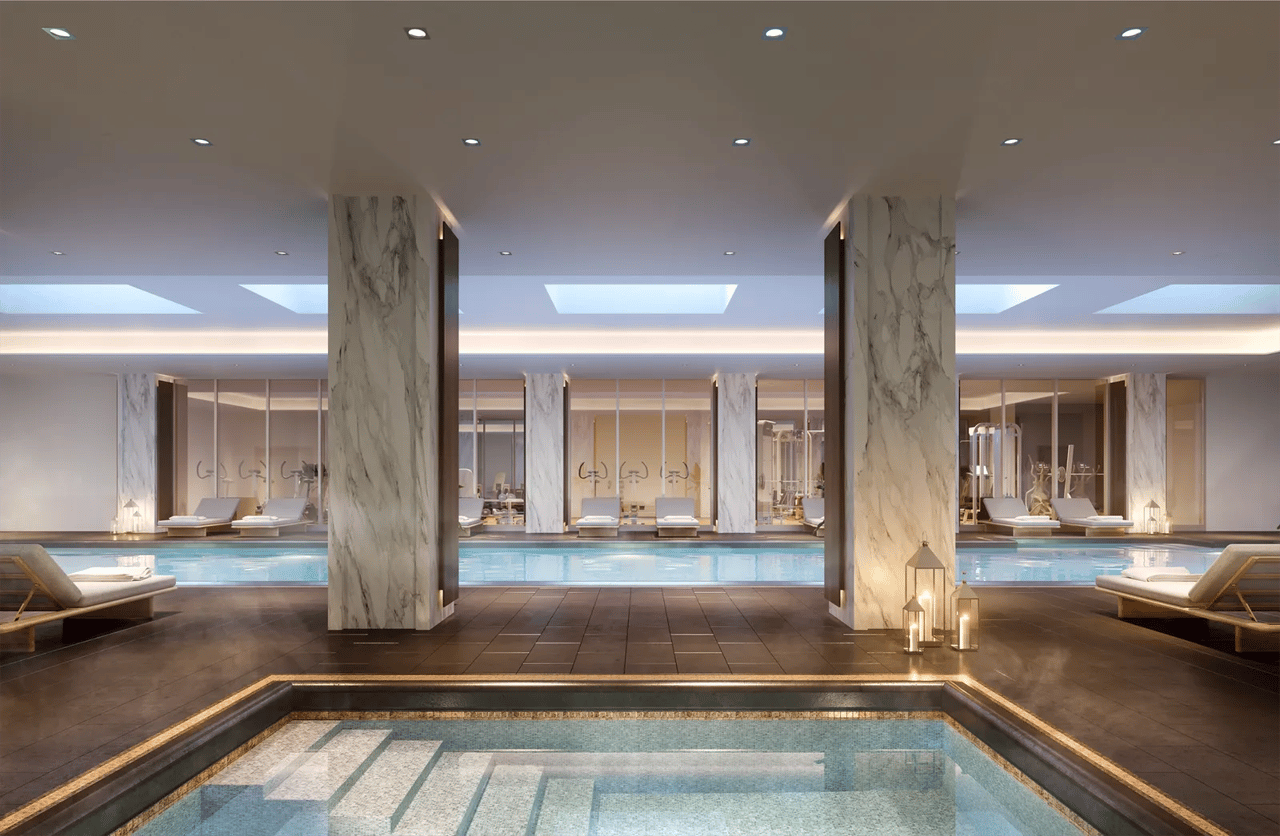 Indoor pool with marble columns, lounge chairs, and a fitness room behind glass walls