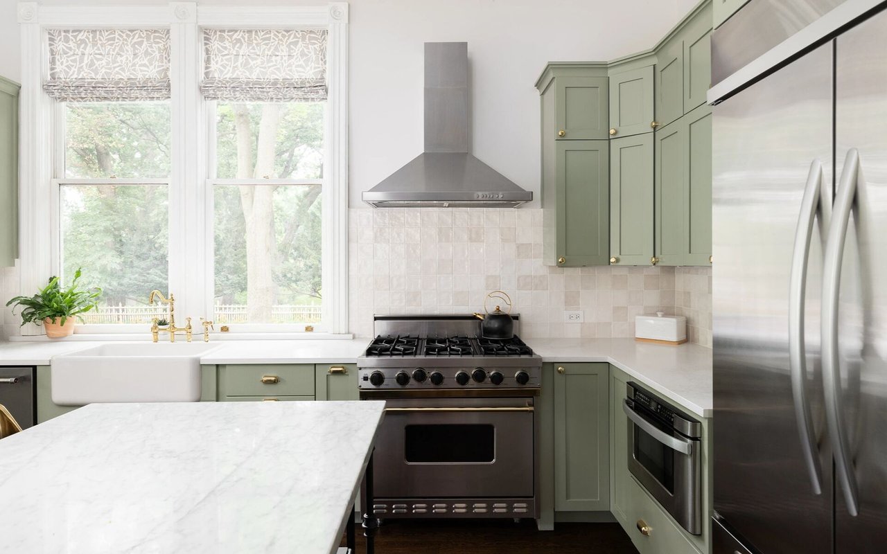 Kitchen with sage-green cabinets, a farmhouse sink beneath tall windows, and a marble island.