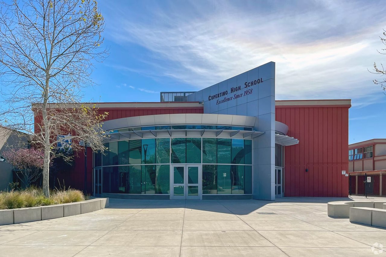Cupertino High School’s red-and-gray entrance with curved glass windows and a broad concrete plaza.