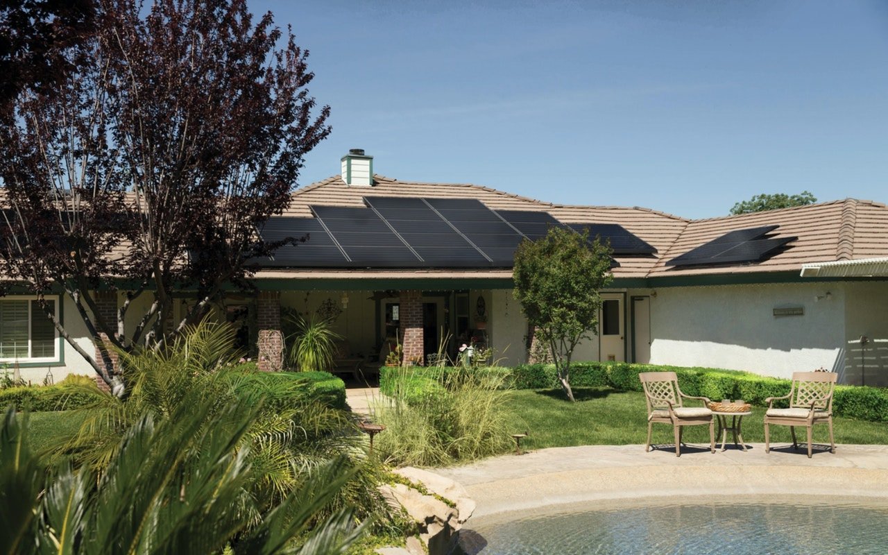 Single-story home with rooftop solar panels, landscaped yard, and poolside seating.