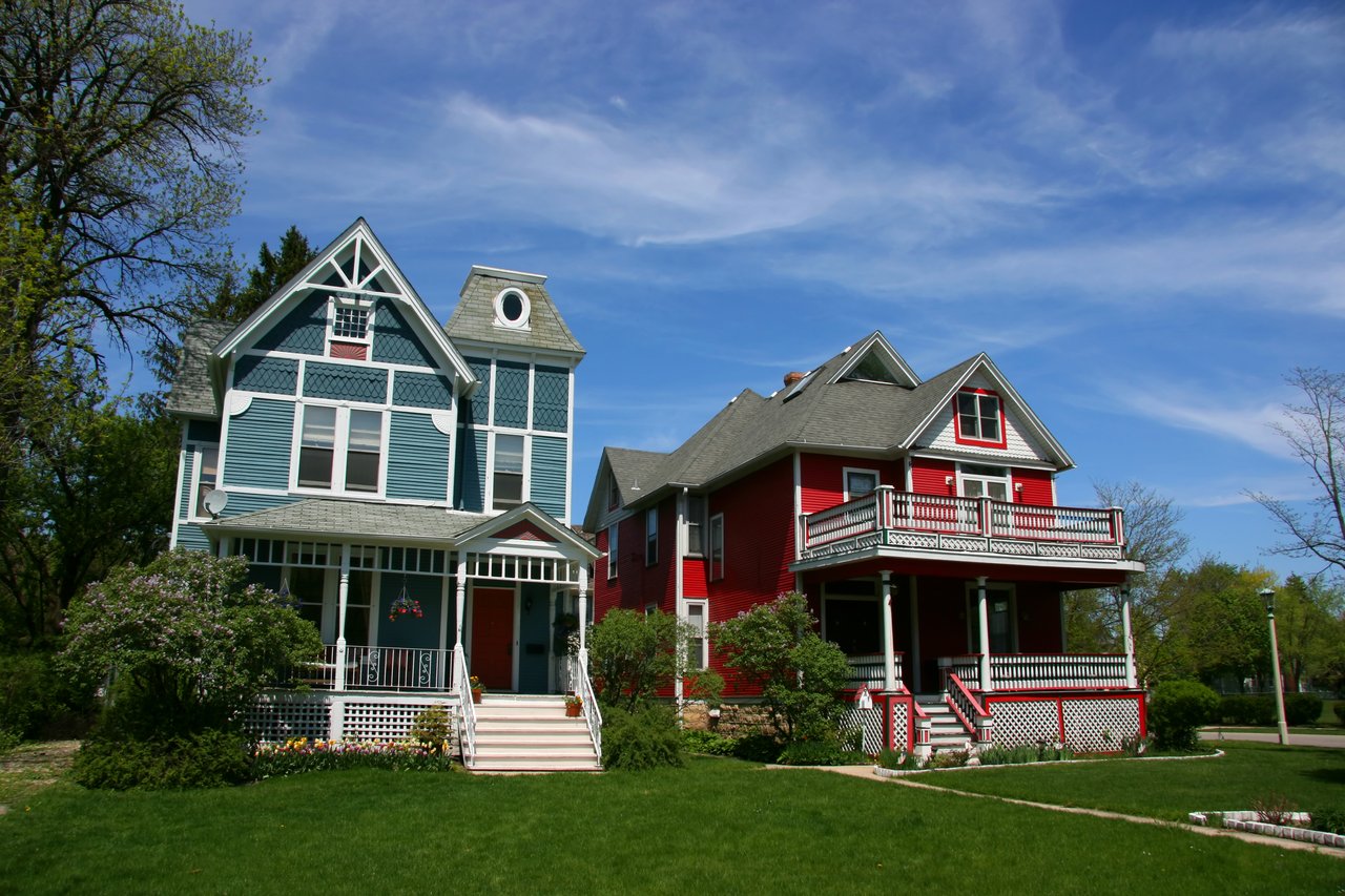 Two Victorian-style homes, one blue and one red, with ornate gables and wraparound porches.