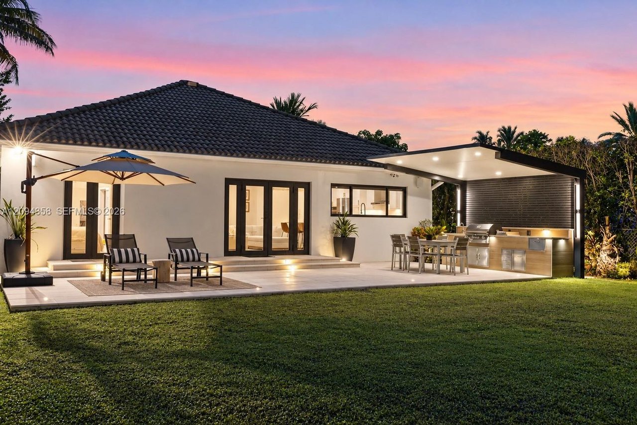Modern single-story home with a tiled roof, patio seating, and an outdoor kitchen at dusk.