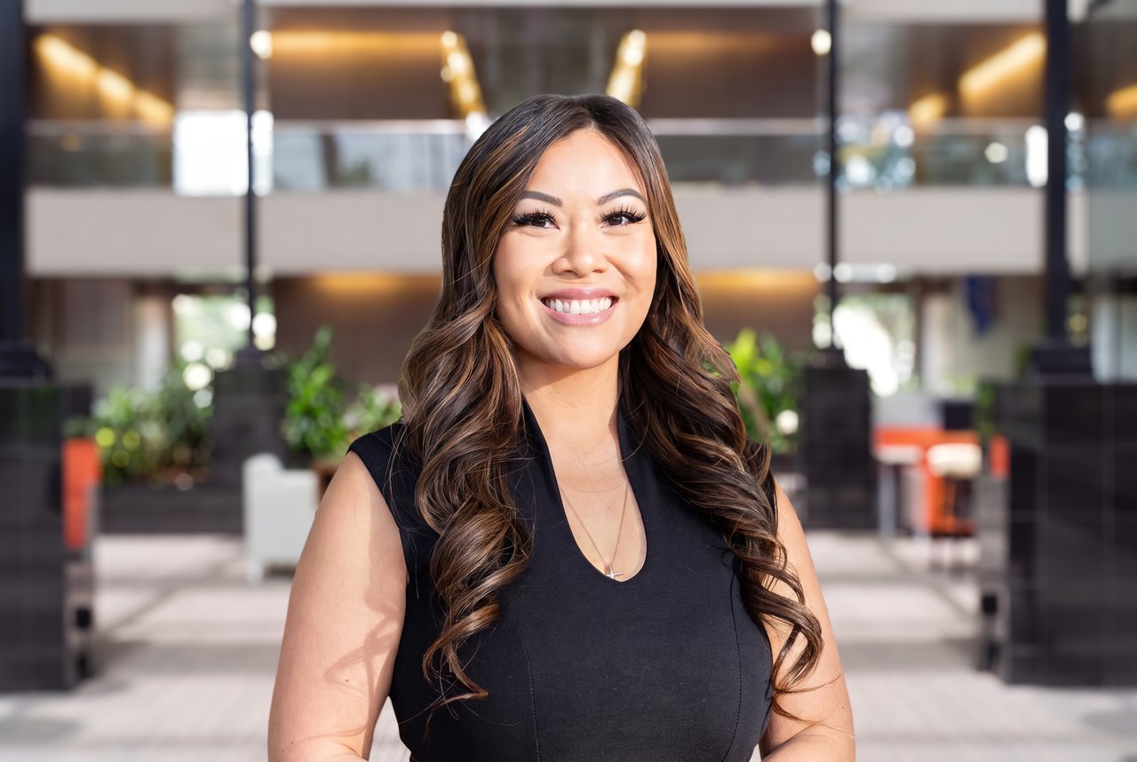 Anh Rodriguez smiling in a black sleeveless top in a modern office lobby.