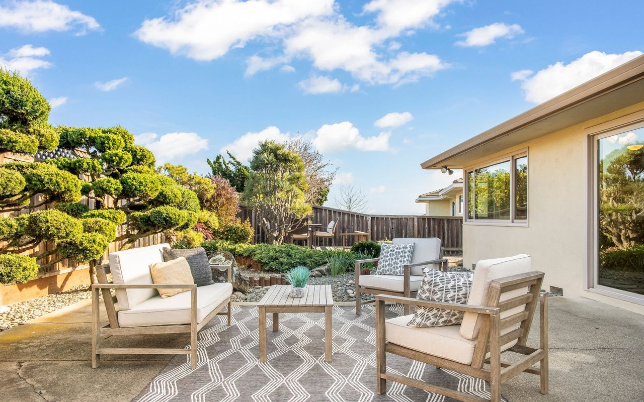 Backyard patio with cushioned seating, a patterned rug, and landscaped garden beds beside the home.