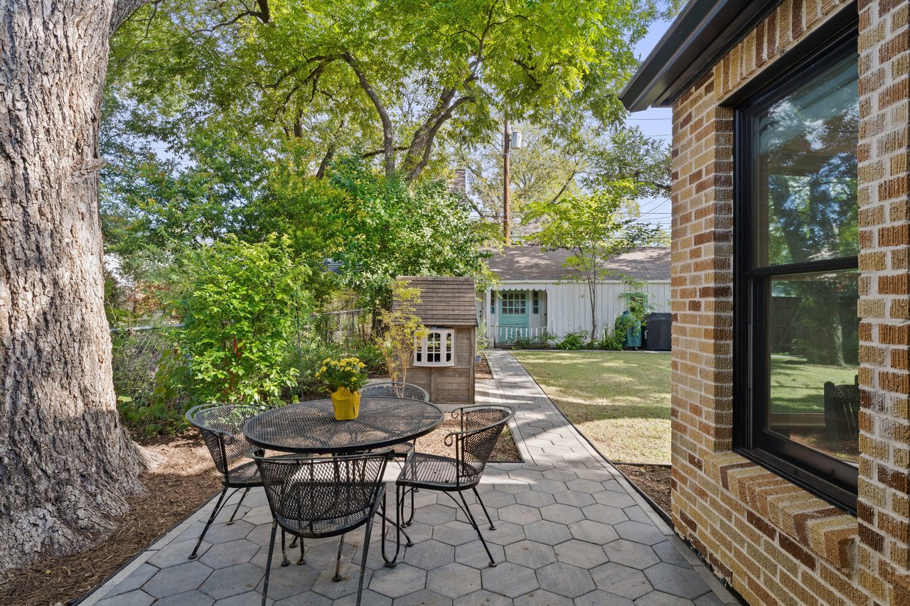 Paved backyard patio with a black metal dining set beneath a large shade tree.