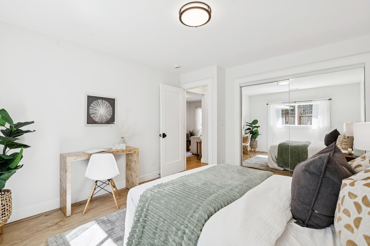 Staged bedroom with a pale green quilt, mirrored closet doors, and a small desk.