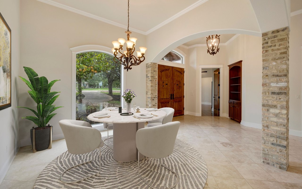 Dining room with an oval table, patterned rug, arched window, and wood double doors.