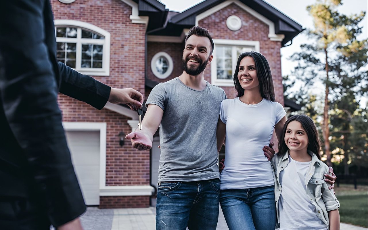 A smiling family receives house keys in front of a two-story brick home.