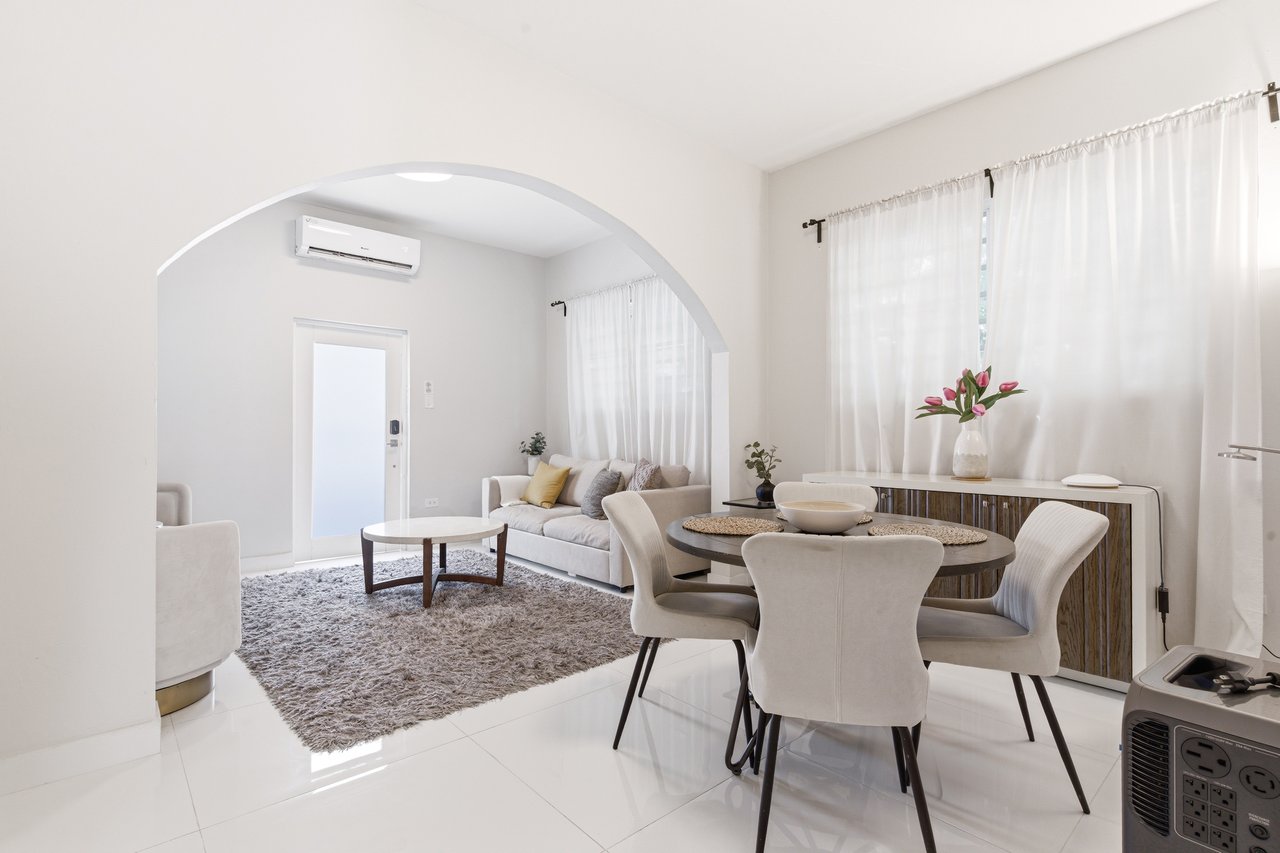 Furnished living and dining area with an arched opening, white sofa, round table, and sheer curtains.