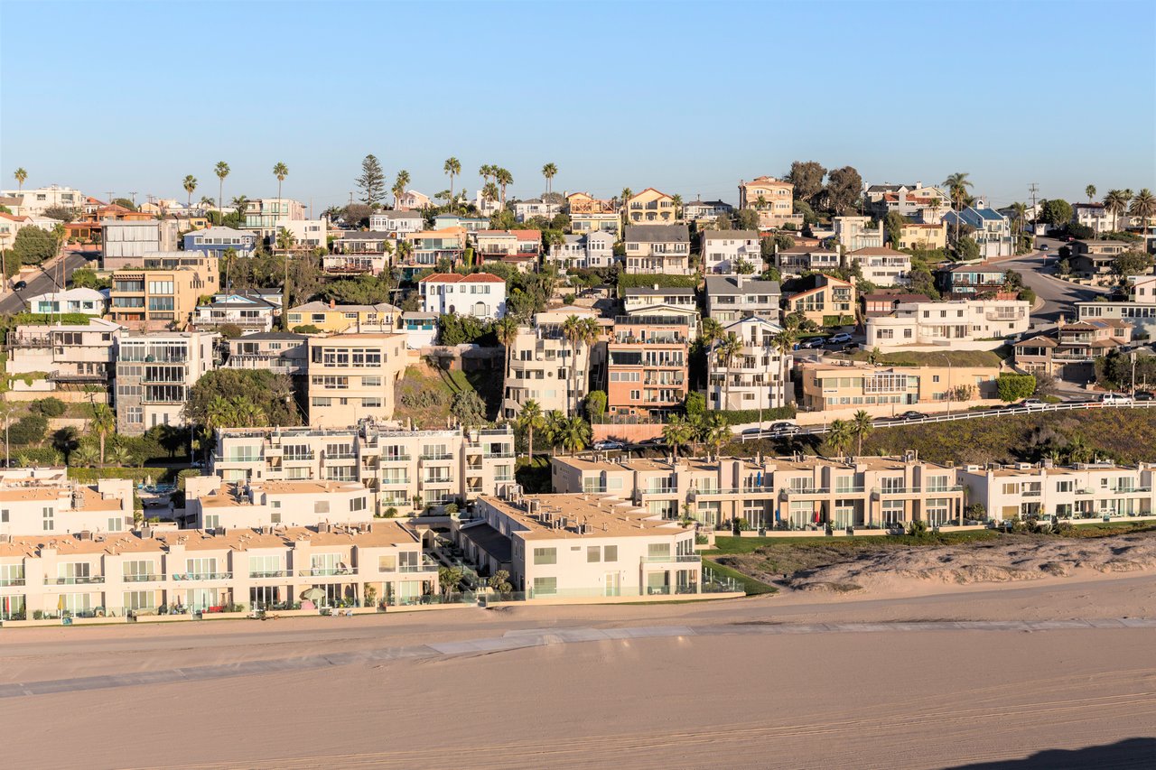 Coastal homes above a sandy beach, with palm trees and hillside residences.