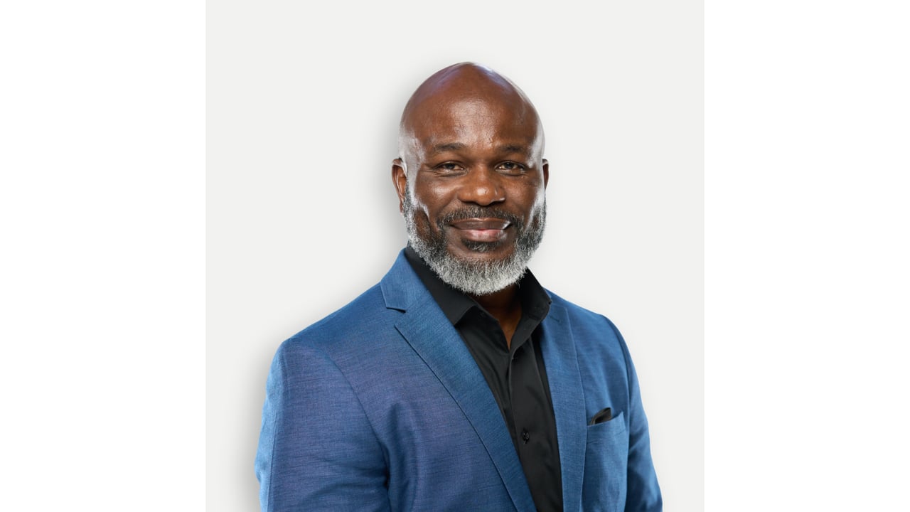 Ikenna Ezeude in a blue blazer and black shirt, with a neatly trimmed gray beard.