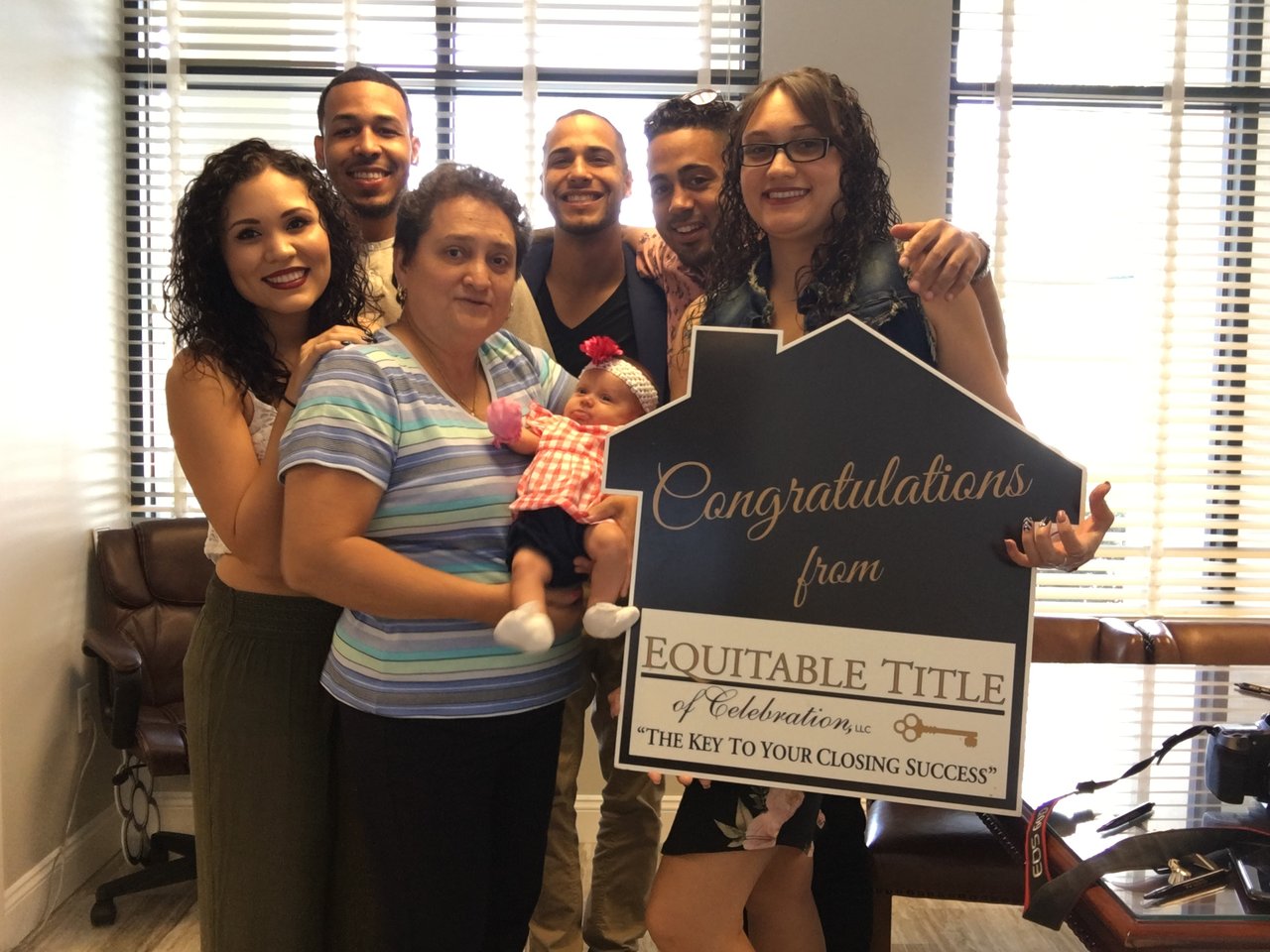 Six adults and a baby pose with a congratulations sign after a closing.