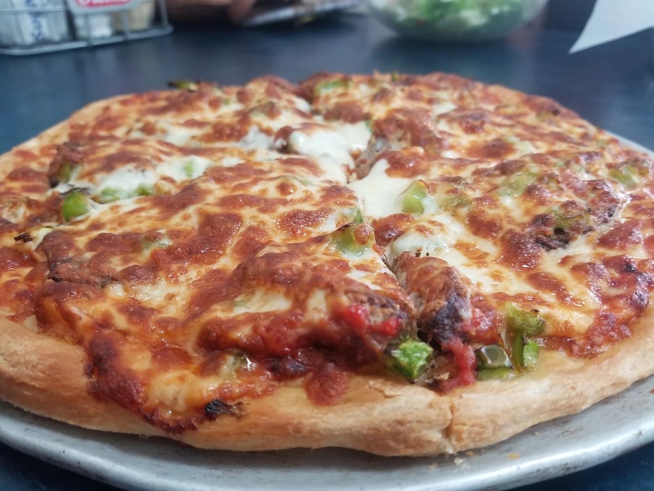 Pizza with browned melted cheese, green peppers, sausage, and tomato on a metal tray.
