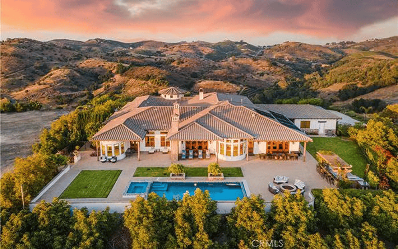 Aerial view of a tiled-roof estate with a swimming pool and rolling hills at sunset.