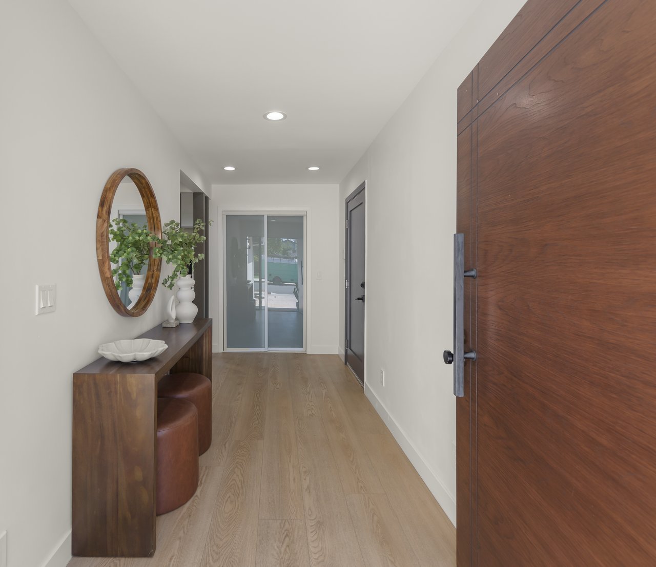 Entry hall with a large wood front door, console table, round mirror, and light wood flooring.