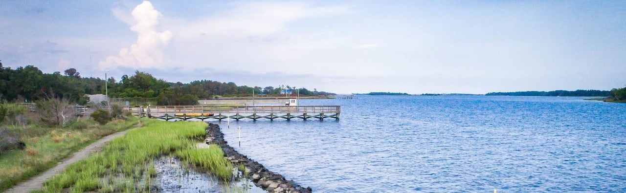 Coastal waterway at Holly Ridge with a wooden pier and grassy marsh shoreline.