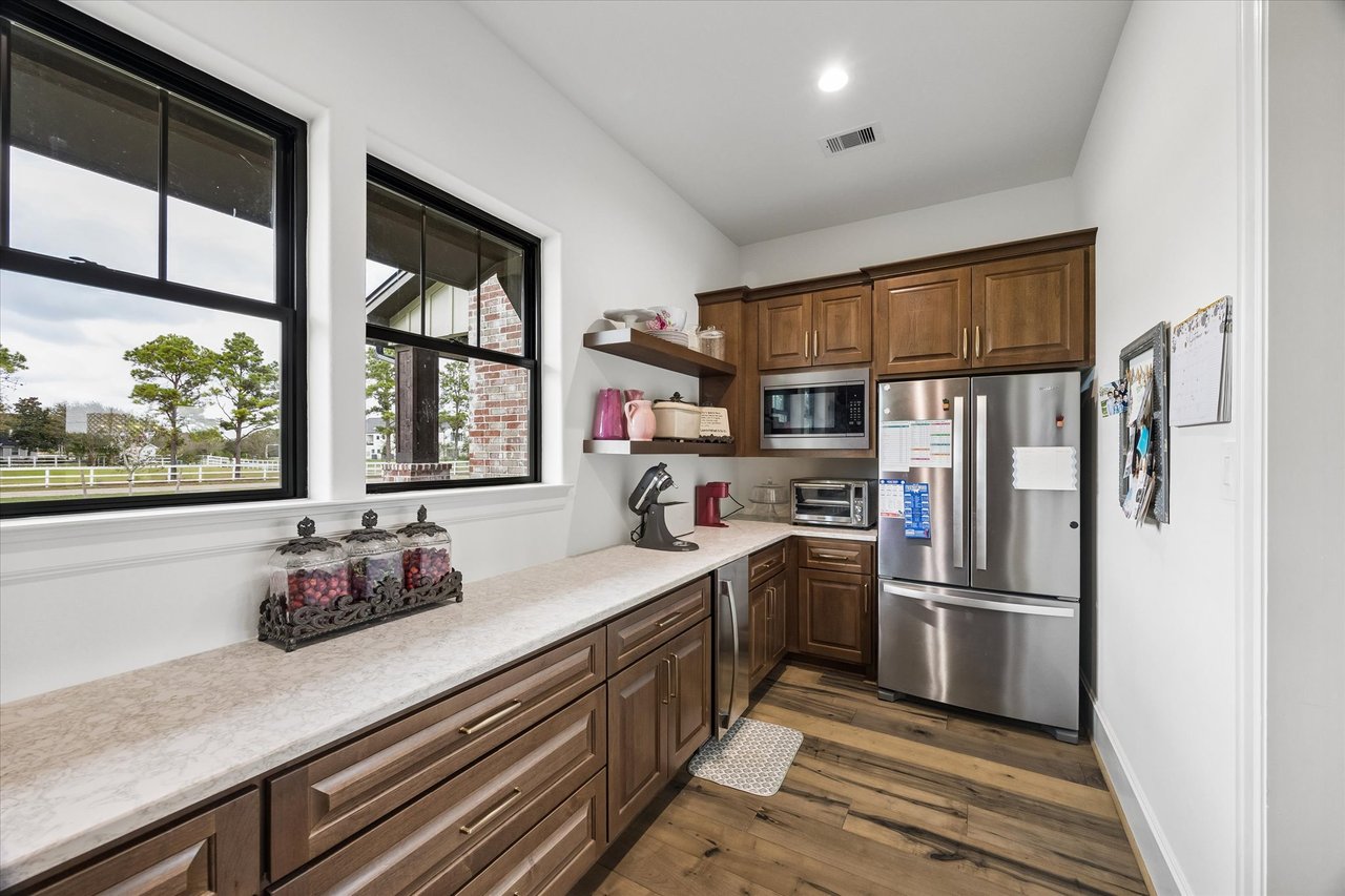 Kitchen with dark wood cabinetry, a long stone counter, stainless appliances, and two large windows.