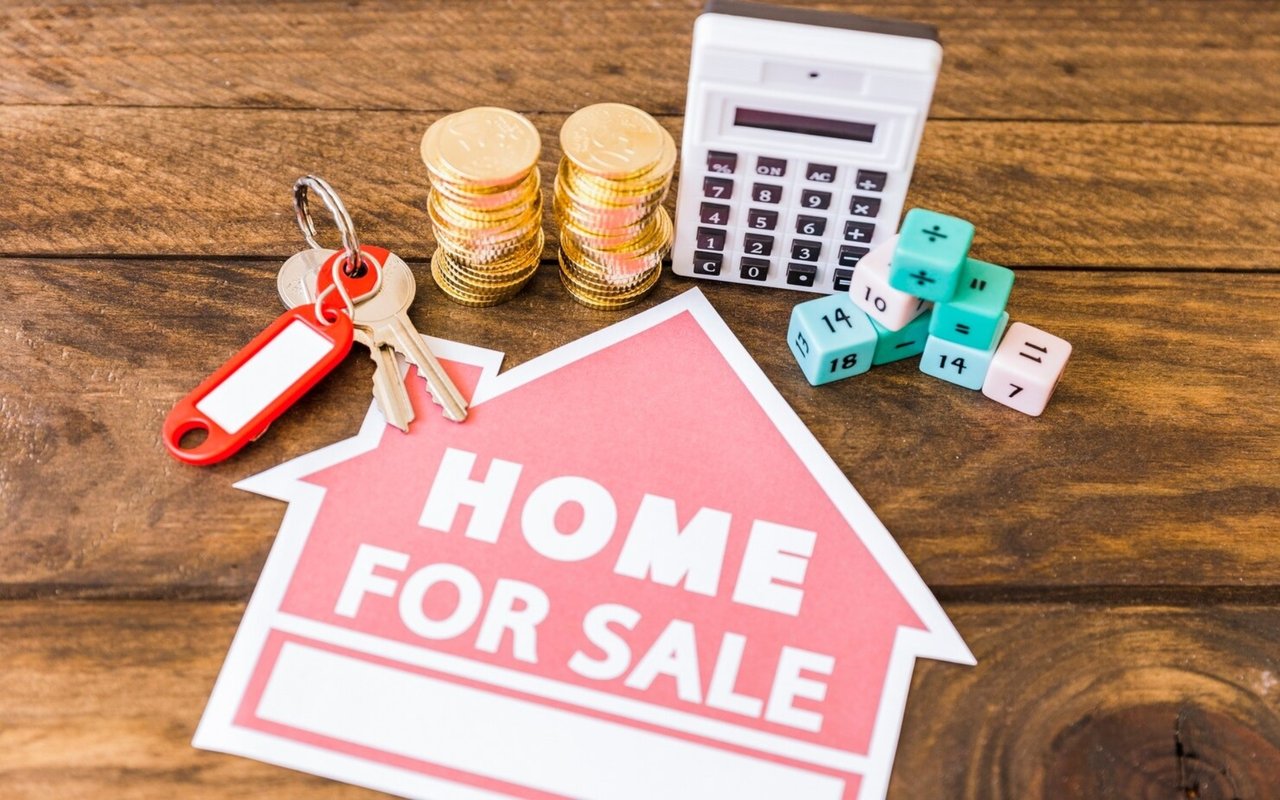 Home-for-sale sign beside keys, coin stacks, a calculator, and numbered blocks.
