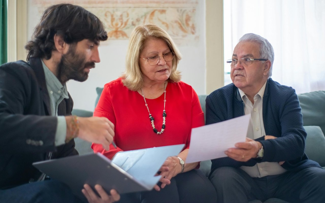 Three adults review paperwork together, with one man holding a document and another pointing it out.